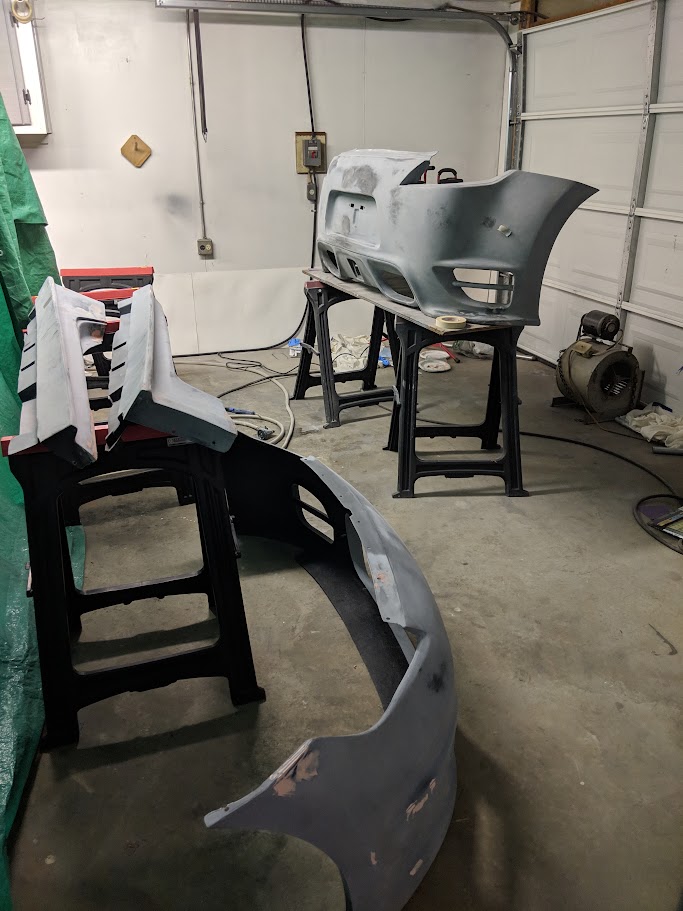 Front and rear bumper covers in gray primer on paint stands in the garage
