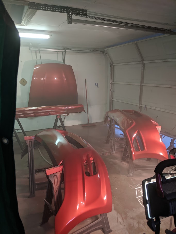 Freshly painted red hood and fender panels drying in the garage